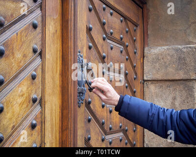 Mann hält Türklopfer aus alte Holztür in der Hand. Er klopft an die verschlossene Tür. Stockfoto