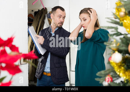 Schuldeneintreiber und traurige junge Frau mit überfälligen Zahlung bei Eingang vor Weihnachten Stockfoto