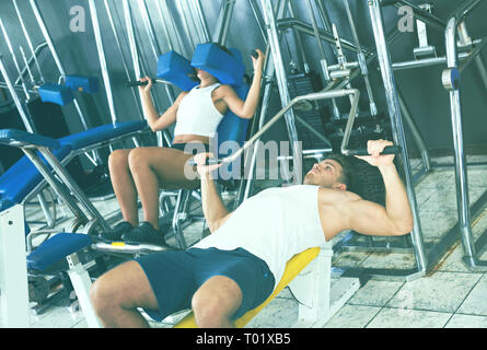 Junge gut ausgebildete Mann, Bankdrücken Übung mit Fitnessraum Maschinen in Innenräumen Stockfoto