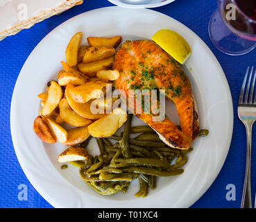 Gebratenes Lachsfilet mit gebackenen Kartoffeln und grüne Bohnen serviert. Stockfoto