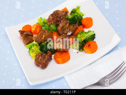 Gebratenes Huhn Herzen mit gekochten Brokkoli und gebackene Karotten auf weiße Platte serviert. Stockfoto