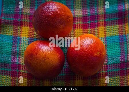 Mehrere frische rote Orangen sind gerade von einem Baum pflücken und gestapelt auf einem karierten Stoff in verschiedenen Farben, die für den Verkauf oder die lecker. Stockfoto