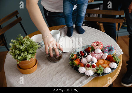 Weibliche Hand hält Kaffeebohnen und speichert von unten fallen. Schöne und bunte Mischung von Zephyr und Früchte auf einem Tisch in der Küche Stockfoto