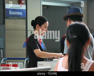 INCHEON, KOREA – AUGUST 2014: Ein Flugbegleiter von Asiana Airlines checkt Passagiere für das Boarding am Incheon International Airport ein. Stockfoto