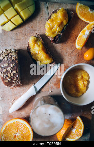 Hausgemachte Orange Marmelade auf einem natürlichen Rohstoff Weizen Brot und Orangenscheiben über eine hölzerne cutboard, gesundes Frühstück, in der Nähe und windom Licht. Stockfoto