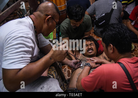 Nakhon Chaisi, Thailand. 16. März 2019. Ein Devotee erhält eine schützende Tattoo auf seinem Rücken während der jährlichen Wat Bang Phra Tattoo Festival in Nakhon Chaisi Bezirk, Thailand, etwa 50 km westlich von Bangkok, am 16. März 2019. Während Tausende von Thais Leute am Schrein im Wat Bang Phra Nakhon Chai Si Region versammelt, (ca. 50 km westlich von Bangkok), um zu sehen, den Wat Bang Phra Tattoo Festival Quelle: PACIFIC PRESS/Alamy leben Nachrichten Stockfoto