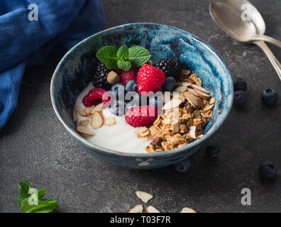 Eine Schüssel mit hausgemachtem Müsli, Joghurt, Mandel Blüten und frischen Beeren. vegetarisches Essen Konzept Stockfoto