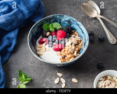 Eine Schüssel mit hausgemachtem Müsli, Joghurt, Mandel Blüten und frischen Beeren. vegetarisches Essen Konzept Stockfoto