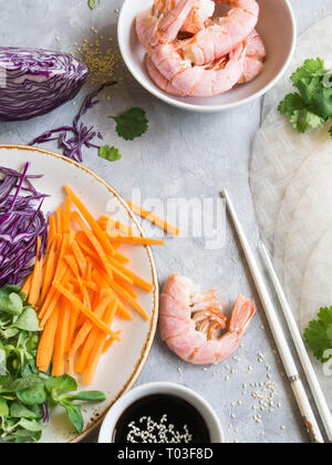 Zutaten zum Kochen Frühlingsrollen - Karotten, Mais Salat, Rotkohl, Garnelen, Reis papier auf grauem Hintergrund Stockfoto