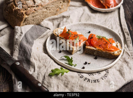 Toast mit geräuchertem Lachs und Frischkäse an Bord auf einem grauen Bettwäsche Handtuch Stockfoto