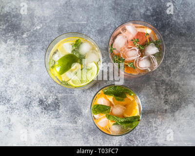 Set Sommer kalte Getränke mit verschiedenen Zitrusfrüchten in Gläsern auf einem grauen Hintergrund. Cocktail mit Grapefruit, Orange, Lemon Lime und Eis Stockfoto