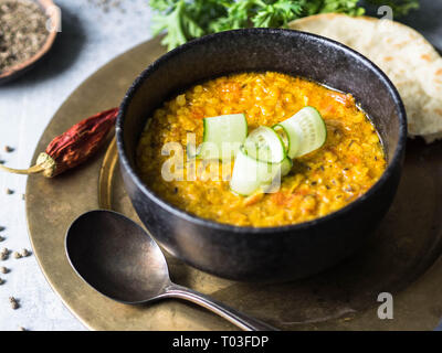Traditionelle indische Linsensuppe Dal Suppe. Heiß und würzig Linsensuppe mit frischen Gurkenscheiben in einem schwarzen Stein Schüssel und Pita Stockfoto