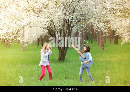 Kinder Rock Band von zwei lustige kleine Mädchen mit Vintage Gitarren und haarbürste als Mikrofon Musik im Frühjahr blühen Park Stockfoto