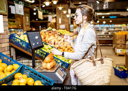 Junge Frau Kunde wiegen die Äpfel im eco Beutel auf der Waage verpackt im Supermarkt Stockfoto