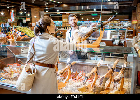 Verkäufer Beratung jamon für eine junge Frau, die Kunden an der Theke stehend mit getrocknetem Fleisch im Supermarkt Stockfoto