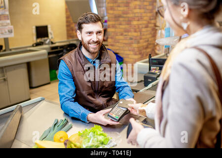 Junge Frau Kunde Zahlung mit einer Kreditkarte für Einkäufe an der Kasse mit fröhlichen Kassierer im Supermarkt Stockfoto