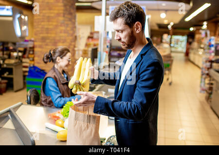 Geschäftsmann kaufen gesunde Lebensmittel, Verpackung Produkte an der Kasse mit fröhlichen Kassierer im Supermarkt Stockfoto