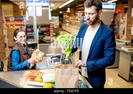 Geschäftsmann kaufen gesunde Lebensmittel, Verpackung Produkte an der Kasse mit fröhlichen Kassierer im Supermarkt Stockfoto