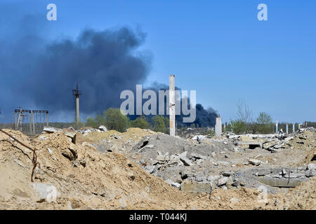 Ein Haufen von betonschutt mit hervorstehenden Armierungseisen auf dem Hintergrund von dichtem schwarzem Rauch in den blauen Himmel. Hintergrund. Das Konzept der Folgen Stockfoto