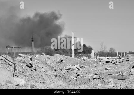 Ein Haufen von betonschutt mit hervorstehenden Armierungseisen auf dem Hintergrund von dichtem schwarzem Rauch in den blauen Himmel. Hintergrund. Das Konzept der Folgen Stockfoto