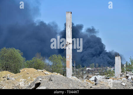 Ein Haufen von betonschutt mit hervorstehenden Armierungseisen auf dem Hintergrund von dichtem schwarzem Rauch in den blauen Himmel. Hintergrund. Das Konzept der Folgen Stockfoto