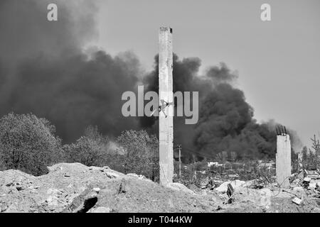 Ein Haufen von betonschutt mit hervorstehenden Armierungseisen auf dem Hintergrund von dichtem schwarzem Rauch in den blauen Himmel. Hintergrund. Das Konzept der Folgen Stockfoto