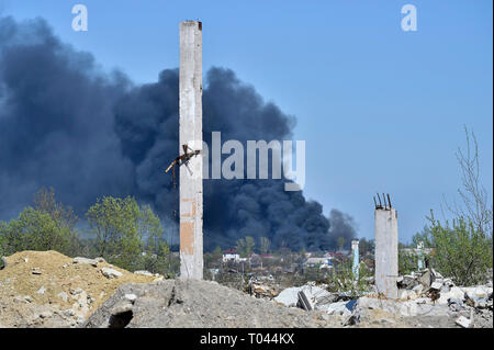 Ein Haufen von betonschutt mit hervorstehenden Armierungseisen auf dem Hintergrund von dichtem schwarzem Rauch in den blauen Himmel. Hintergrund. Das Konzept der Folgen Stockfoto