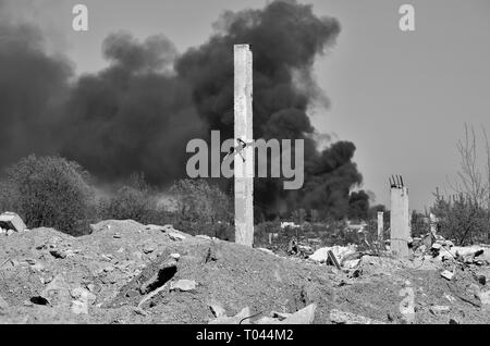 Ein Haufen von betonschutt mit hervorstehenden Armierungseisen auf dem Hintergrund von dichtem schwarzem Rauch in den blauen Himmel. Hintergrund. Das Konzept der Folgen Stockfoto