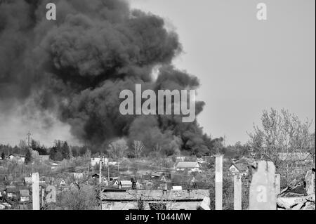 Ein Haufen von betonschutt mit hervorstehenden Armierungseisen auf dem Hintergrund von dichtem schwarzem Rauch in den blauen Himmel. Hintergrund. Das Konzept der Folgen Stockfoto