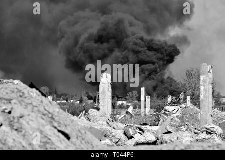 Ein Haufen von betonschutt mit hervorstehenden Armierungseisen auf dem Hintergrund von dichtem schwarzem Rauch in den blauen Himmel. Hintergrund. Das Konzept der Folgen Stockfoto