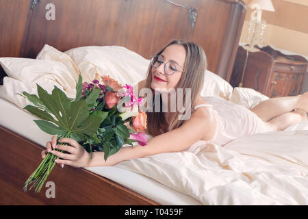 Junge Frau mit einem Blumenstrauß im Bett Stockfoto