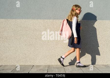 Eine Schülerin der Grundschule mit Notebooks in der Hand. Ein Mädchen mit einem Rucksack geht in die Schule. Zurück zur Schule Stockfoto