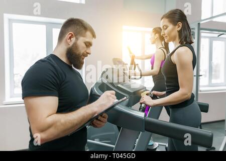 Junge lächelnde fitness Frauen mit Personal Trainer ein Erwachsener athletischen Mann auf Laufband im Fitnessstudio. Sport, Teamarbeit, Training, gesunden Lebensstil Konzept. Stockfoto