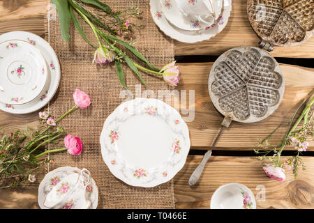 Alte romantische Porzellan, rosa Blumen und alten Waffeleisen auf rustikale Holzplanken angeordnet. Von oben, flach Schuß. Stockfoto