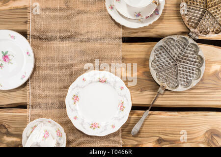 Alte romantische Porzellan und alten Waffeleisen auf rustikale Holzplanken angeordnet. Von oben, flach Schuß. Stockfoto