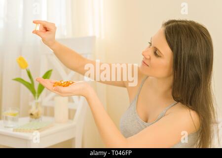 Junge schöne Frau morgens im Bett sitzen Vitamine nimmt, Fischöl omega-3 Vitamin E. Frühling, gesunde Lebensweise und Ernährung Stockfoto