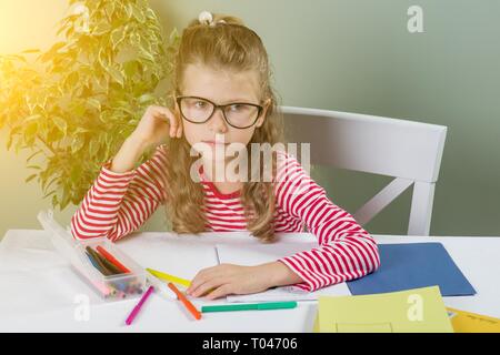 Traurig und müde niedlich junior Schülerin mit blonden Haaren in Stress arbeiten Hausaufgaben sitzen gelangweilt und in den Kindern Bildung überwältigt bei s Stockfoto