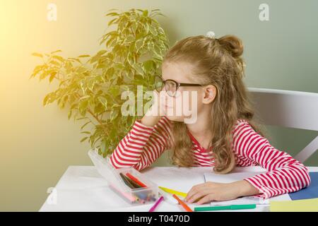 Traurig und müde niedlich junior Schülerin mit blonden Haaren in Stress arbeiten Hausaufgaben sitzen gelangweilt und in den Kindern Bildung überwältigt bei s Stockfoto