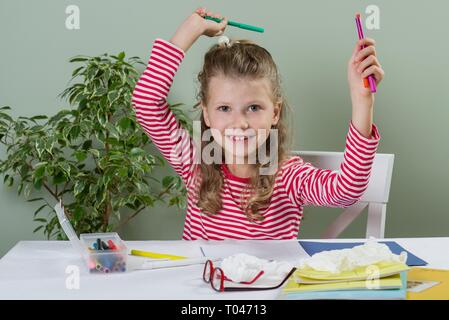 Niedlich junior Schülerin mit blonden Haaren, lächelnd, Zeichnung in einer Schule Notebook und Spaß zu Hause an einem Tisch Stockfoto