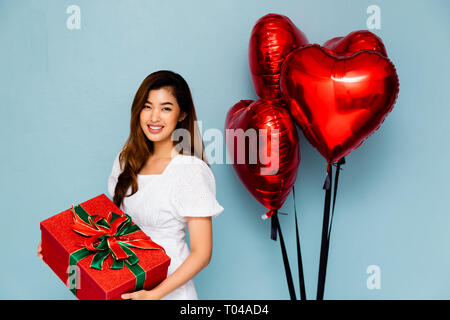 Schöne Thai Frauen mit schön verpackt präsentieren lächelnd und mit Blick auf die Kamera beim Stehen in der Nähe von Bündel Luftballons auf blauem Hintergrund Stockfoto