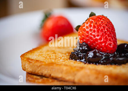 Tischplatte in der Nähe von Brot Toast mit dem Belag der Cranberry Konfitüre und Erdbeere im weißen Platte am Esstisch aus Holz. Stockfoto