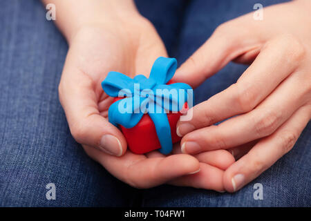 Frau hält Geschenk mit blauer Schleife umwickelt. Geschenkbox und Band sind aus Lehm gemacht (Knetmasse). Close Up. Stockfoto