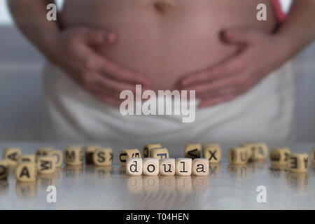 Wort DOULA aus Holz Buchstaben. Schwangere Frau im Hintergrund Stockfoto
