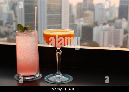 Zwei verschiedene Arten von Cocktails an der Bar auf der Dachterrasse mit verschwommenen Wolkenkratzer im Hintergrund Stockfoto