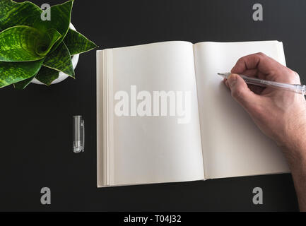 Person schreiben in Buch auf schwarzen Hintergrund mit Topfpflanzen Stockfoto