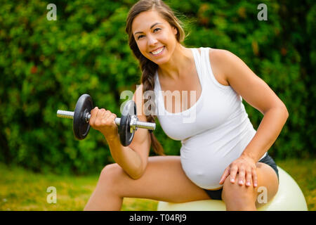 Glücklich schwanger Frauen Training mit Kurzhanteln auf Yoga Ball Stockfoto