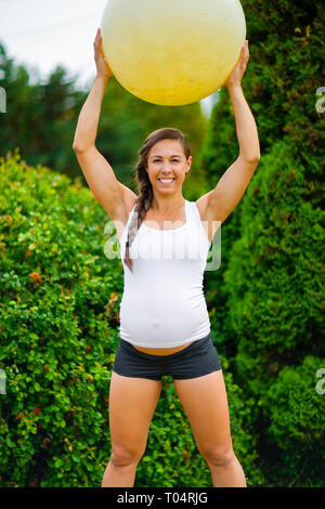 Schwangere Frau lächelnd während des Trainings mit Fitness Ball im Park Stockfoto