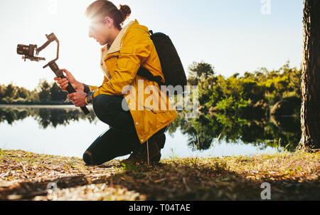 Ein Mann, der fortschrittliche Technik nutzt, um Fotos von der Natur zu machen. Reisende, die neben einem See sitzen und ein Foto mit einer dslr-Kamera machen, die an einer Hand befestigt ist Stockfoto