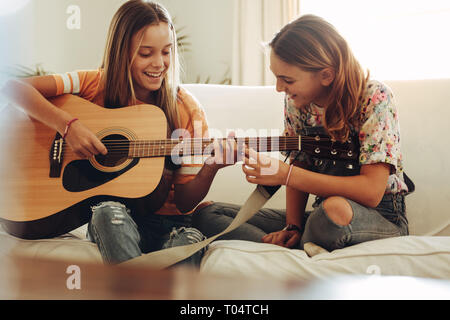 Zwei lächelnde Mädchen lernen Gitarre zu Hause zu spielen. Mädchen, die Musik auf der Gitarre zu Hause. Stockfoto