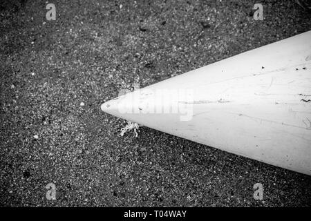 Kajak aus weißem Fiberglas Kunststoff mit im Alter von Markierungen auf dem Strand mit schwarzem Sand und Steine am Meer mit keine Menschen, Hintergrund mit Copyspace Stockfoto
